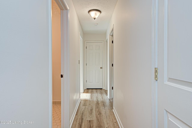 hallway with light wood finished floors, a textured ceiling, and baseboards