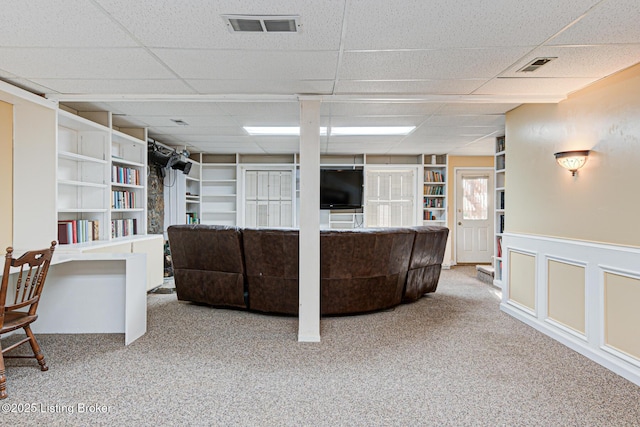 carpeted living room featuring visible vents, wainscoting, a decorative wall, and built in features