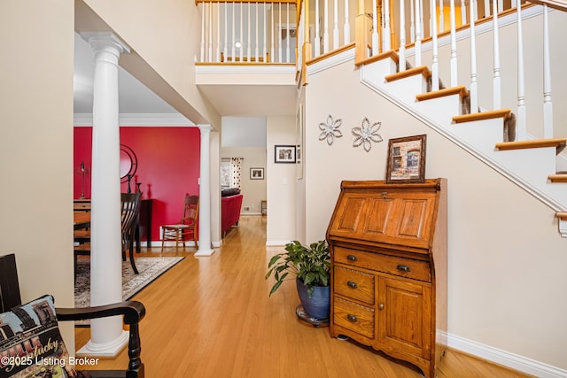 foyer with baseboards, ornate columns, a high ceiling, stairs, and light wood-type flooring