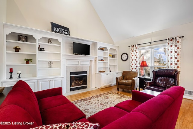 living room featuring high vaulted ceiling, visible vents, light wood finished floors, and a tile fireplace