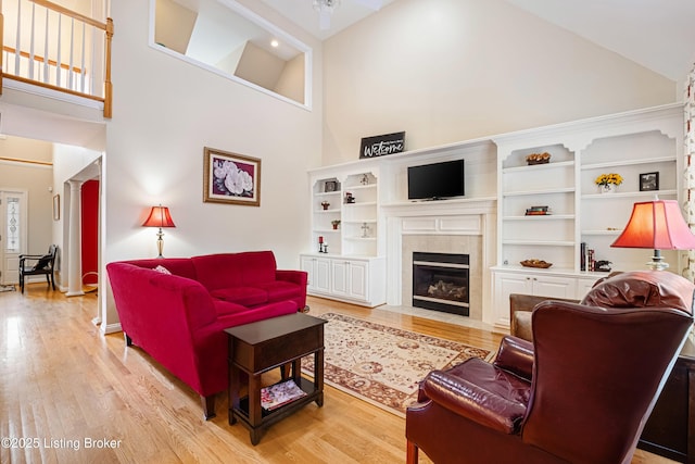 living area featuring high vaulted ceiling, decorative columns, light wood-style floors, and a tiled fireplace