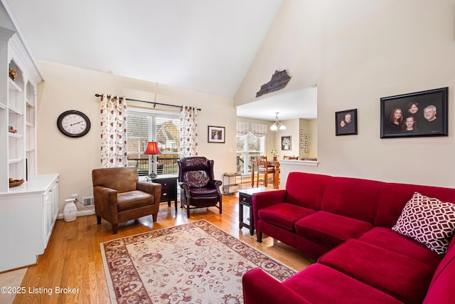 living area featuring high vaulted ceiling, an inviting chandelier, and light wood-style flooring