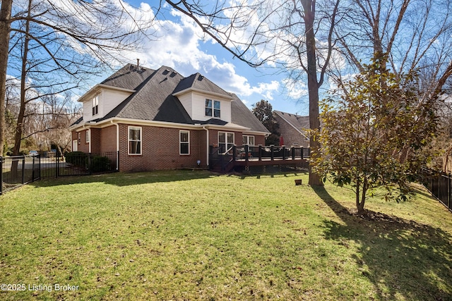 rear view of house with brick siding, roof with shingles, a fenced backyard, a yard, and a deck