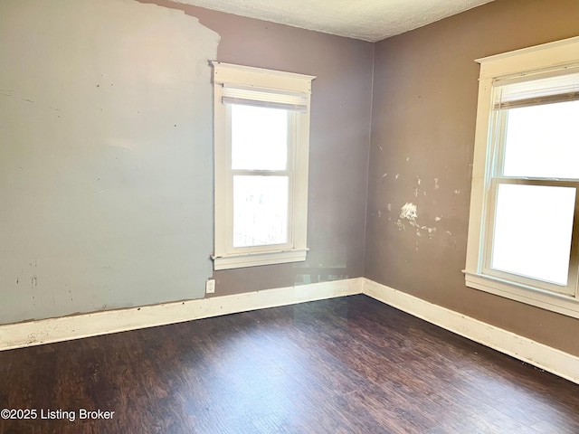 empty room with dark wood finished floors, a textured ceiling, and baseboards