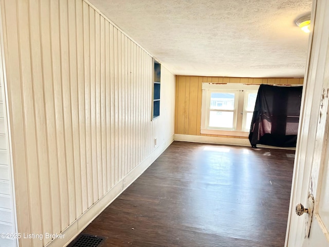 unfurnished room featuring wooden walls, a textured ceiling, and dark wood-type flooring