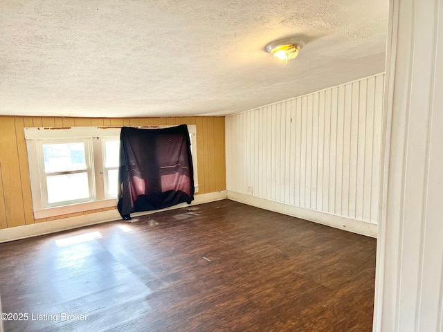 spare room featuring baseboards, a textured ceiling, dark wood-style floors, and wooden walls