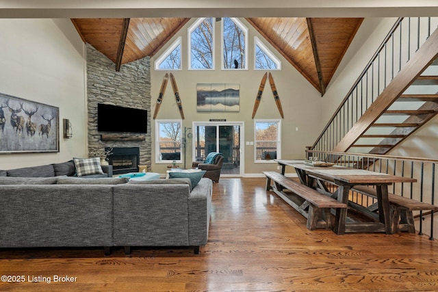 living area featuring a stone fireplace, stairway, wood ceiling, and wood finished floors