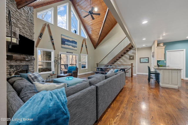 living room featuring a stone fireplace, stairway, plenty of natural light, and wood finished floors