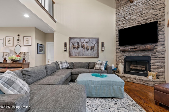 living room featuring a stone fireplace, wood finished floors, and a towering ceiling