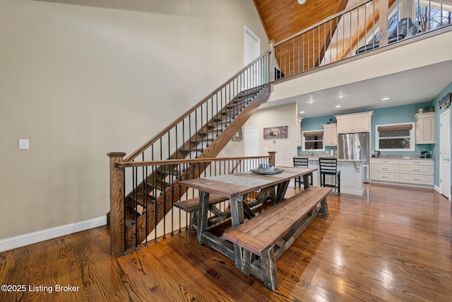 dining space featuring wood finished floors, baseboards, stairs, a towering ceiling, and wooden ceiling