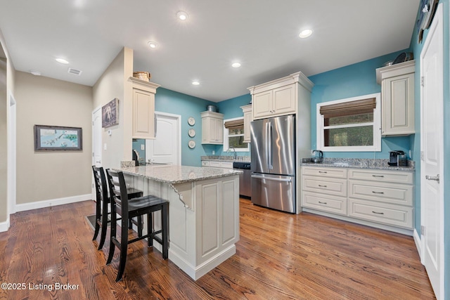 kitchen featuring light stone countertops, a breakfast bar, a peninsula, stainless steel appliances, and light wood-style floors