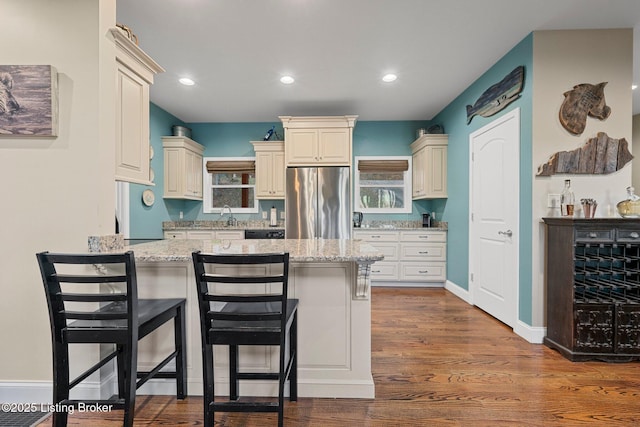 kitchen with light stone counters, stainless steel fridge, a peninsula, and a kitchen breakfast bar