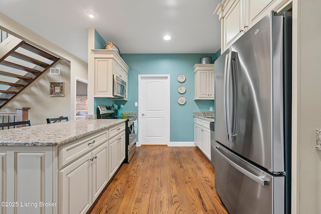 kitchen with wood finished floors, baseboards, visible vents, light stone countertops, and stainless steel appliances