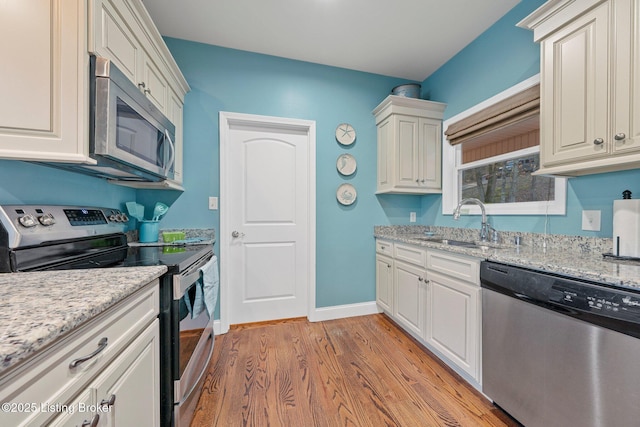 kitchen with light stone counters, baseboards, a sink, appliances with stainless steel finishes, and light wood-type flooring