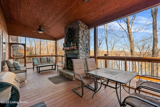 wooden terrace with outdoor dining space, a ceiling fan, and an outdoor living space with a fireplace