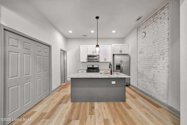 kitchen featuring an island with sink, appliances with stainless steel finishes, light wood-style flooring, and white cabinetry