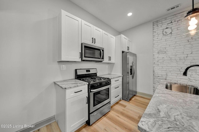 kitchen with visible vents, light wood-style flooring, stainless steel appliances, and a sink