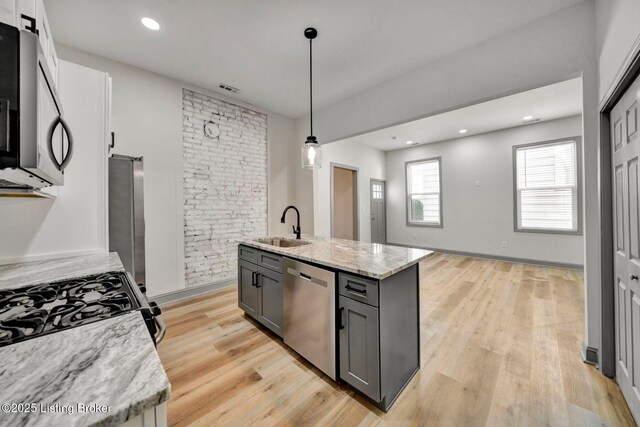 kitchen with a barn door, light stone counters, light wood-style flooring, stainless steel appliances, and a sink