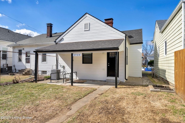 rear view of property featuring roof with shingles, central AC unit, a chimney, a yard, and a patio area