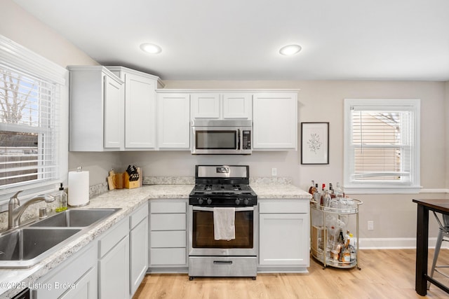 kitchen with appliances with stainless steel finishes, light wood-type flooring, baseboards, and a sink