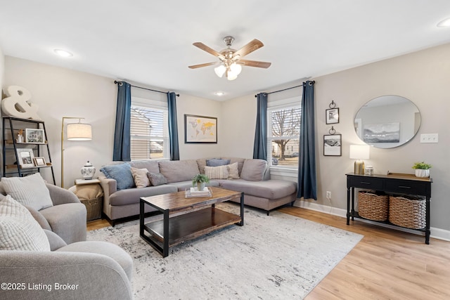 living area with a ceiling fan, light wood-style floors, baseboards, and a wealth of natural light