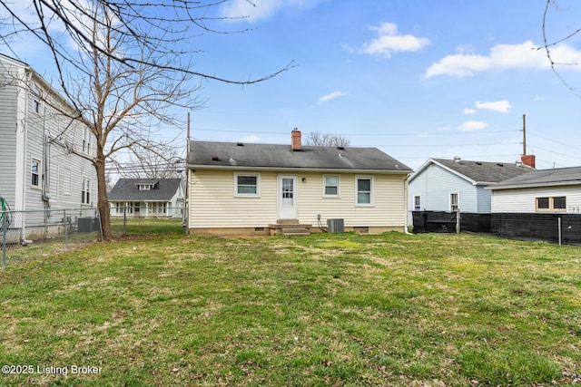 rear view of house featuring entry steps, a lawn, a fenced backyard, and a chimney