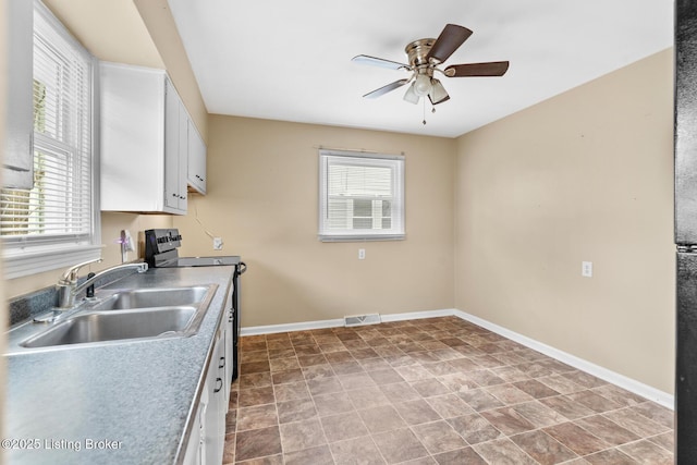 kitchen featuring baseboards, stainless steel range with electric stovetop, white cabinetry, a ceiling fan, and a sink