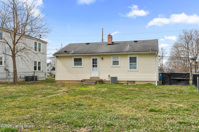 back of property with central AC unit, a lawn, a chimney, and fence