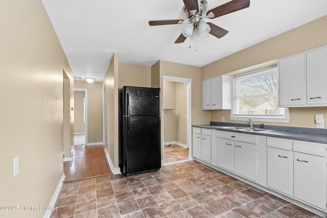 kitchen featuring a ceiling fan, freestanding refrigerator, a sink, white cabinetry, and dark countertops