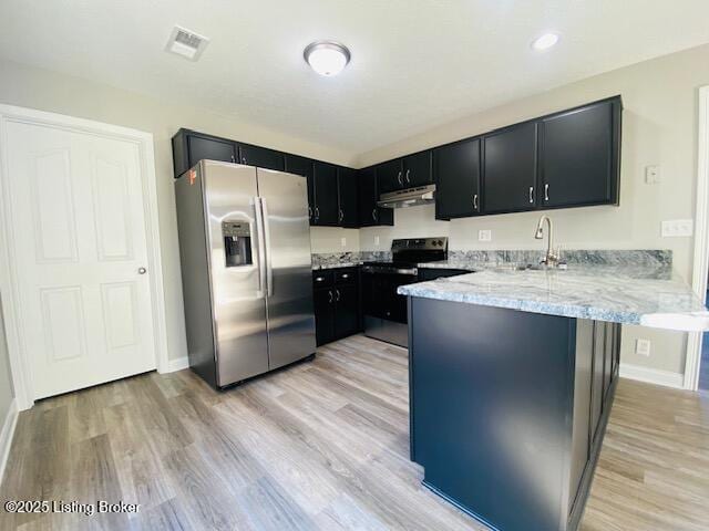 kitchen with a sink, under cabinet range hood, stainless steel appliances, a peninsula, and dark cabinets