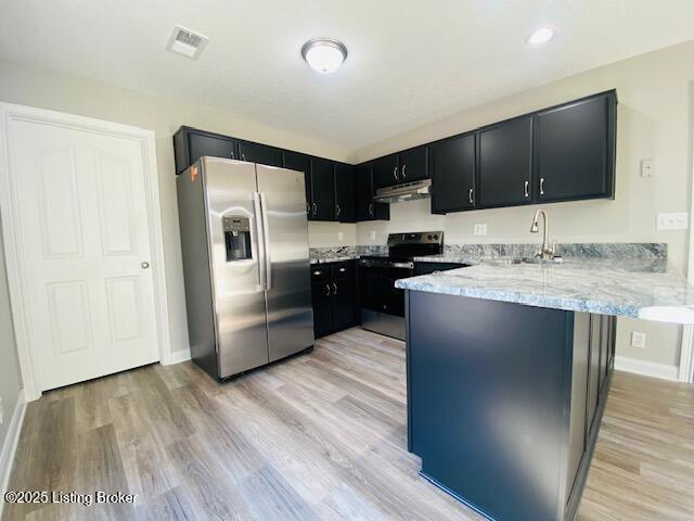 kitchen featuring a peninsula, a sink, stainless steel appliances, under cabinet range hood, and dark cabinets