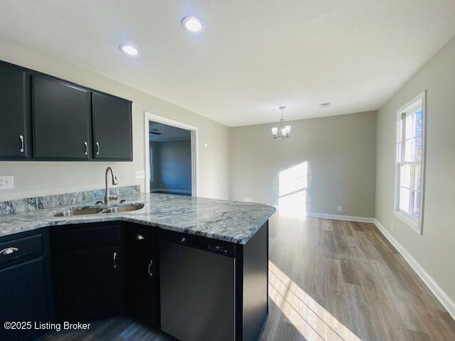 kitchen featuring a sink, wood finished floors, dark cabinetry, a peninsula, and dishwasher