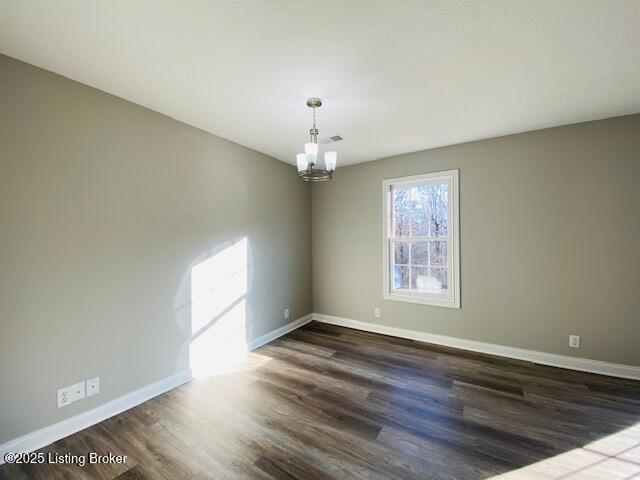 empty room with visible vents, baseboards, a notable chandelier, and dark wood-style flooring