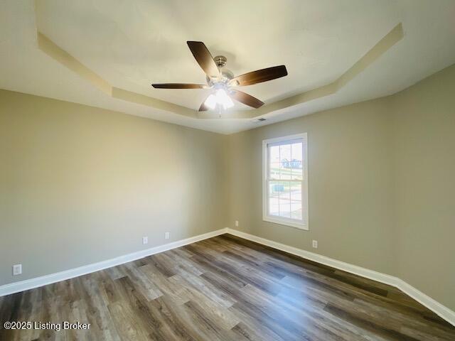 spare room featuring dark wood-style floors, a ceiling fan, a raised ceiling, and baseboards