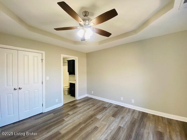 unfurnished bedroom featuring baseboards, dark wood-style flooring, ceiling fan, a closet, and a raised ceiling