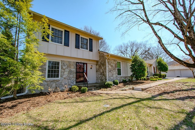 view of front of property featuring a front yard, a detached garage, board and batten siding, and stone siding