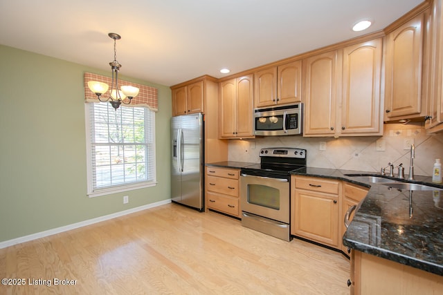 kitchen with light brown cabinets, light wood finished floors, stainless steel appliances, backsplash, and a chandelier