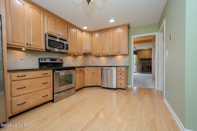 kitchen with dark countertops, appliances with stainless steel finishes, light wood-style flooring, and light brown cabinetry