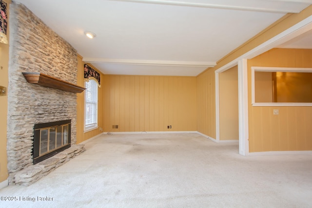 unfurnished living room with beamed ceiling, baseboards, a stone fireplace, and carpet flooring