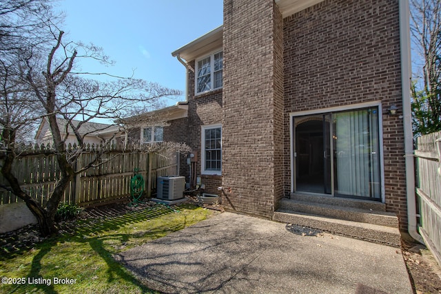 doorway to property featuring a patio, cooling unit, fence, and brick siding