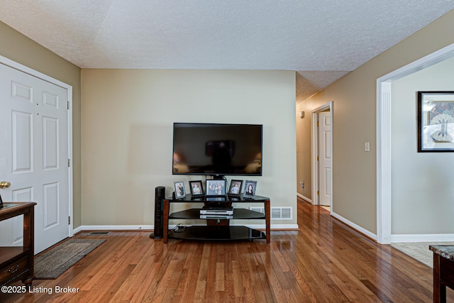 living room with hardwood / wood-style floors, baseboards, visible vents, and a textured ceiling