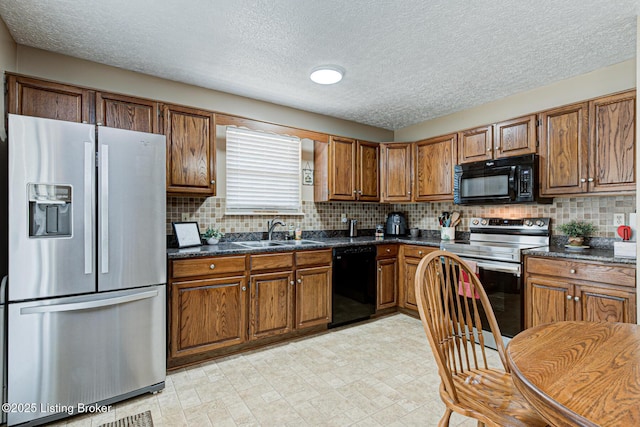 kitchen with dark countertops, backsplash, brown cabinets, black appliances, and a sink