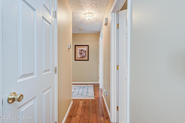 corridor with hardwood / wood-style flooring, baseboards, and a textured ceiling