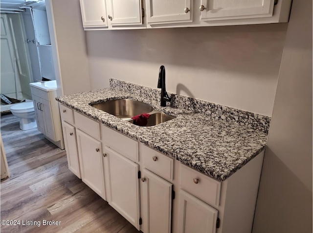 kitchen featuring white cabinetry, stone countertops, light wood finished floors, and a sink