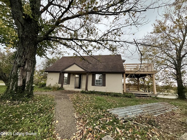 view of front of house featuring a wooden deck, a front yard, and a shingled roof