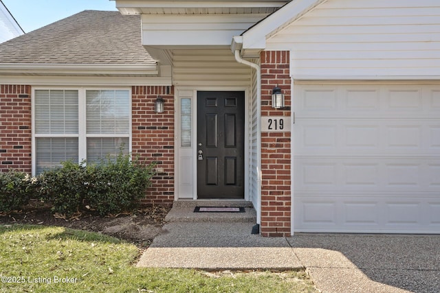 doorway to property with brick siding, a garage, and roof with shingles