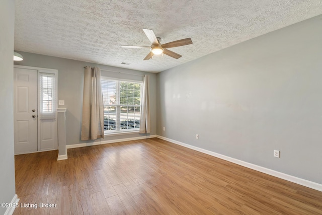 empty room featuring visible vents, a ceiling fan, a textured ceiling, wood finished floors, and baseboards