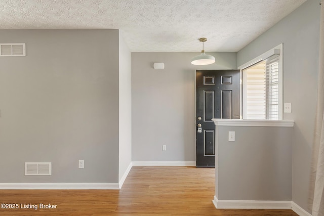 foyer entrance with visible vents, a textured ceiling, baseboards, and light wood-style floors