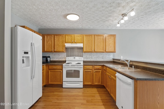 kitchen featuring dark countertops, under cabinet range hood, light wood-style flooring, white appliances, and a sink