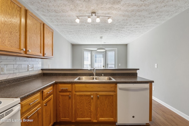 kitchen featuring white appliances, brown cabinets, a peninsula, a sink, and tasteful backsplash